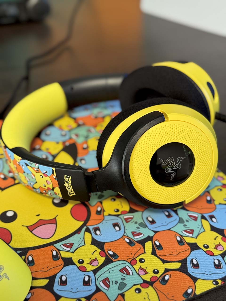 Casque Razer Kraken V4X édition Pokémon en jaune et noir, posé sur un tapis aux motifs des starters de Kanto